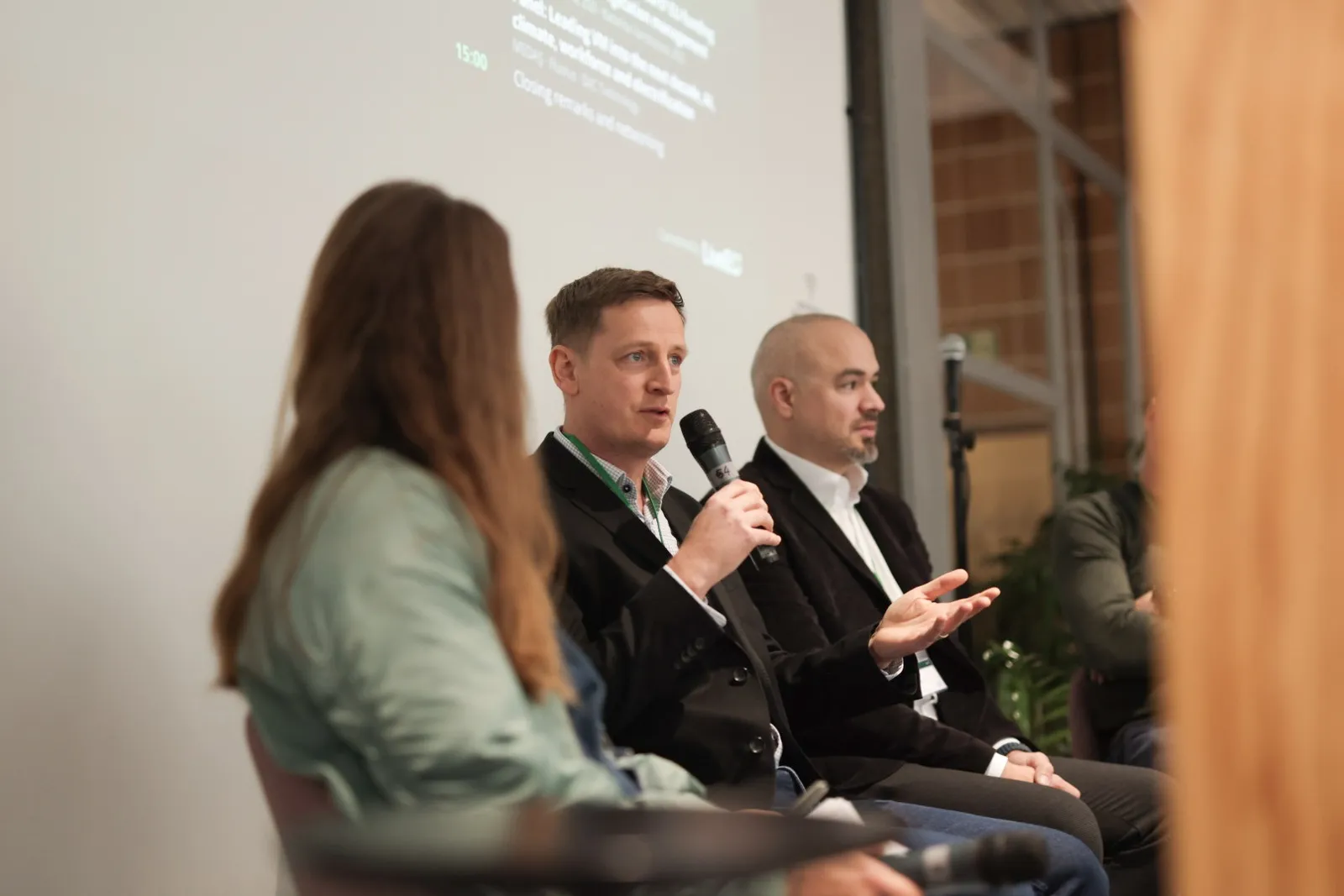 Three panellists seated on stage, one speaking into a microphone